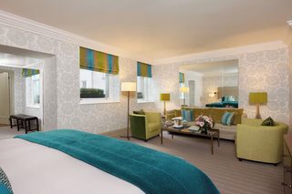A hotel room with a large bed, two armchairs, a sofa, a coffee table, and a mirror.