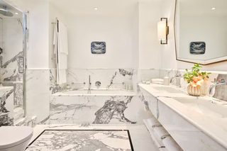 A modern bathroom with a marble floor, a freestanding bathtub, a large mirror, and a vanity with a sink and towel rack.