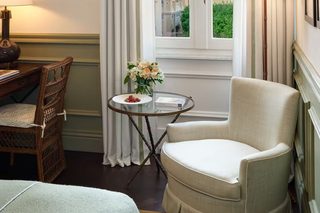 A room with a large window, a chair, a small table with a vase, and a lamp.