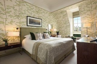 A hotel room with a large bed, a desk, and a chair. There is a window providing natural light and a view of the outside.