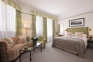 A hotel room with a bed, a sofa, a chair, a nightstand, and a lamp.