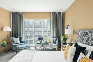 A hotel room with a bed, a sofa, a small table, a lamp, and a view of the city.