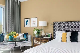 A hotel room with a bed, a sofa, a table with a vase of flowers, a lamp, and framed pictures on the wall.