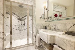 A bathroom with a glass-enclosed shower, a marble sink, and a mirror with a rose vase.