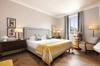 A hotel room with a large bed, two bedside tables with lamps, a chair, and a view of the city through the window.