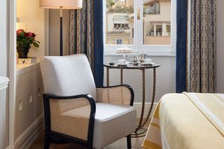 A hotel room with a chair, a small table with a lamp, and a bed.