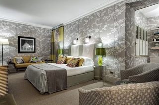 A hotel room with a bed, a sofa, a chair, a lamp, and a mirror.