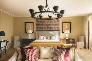A hotel room with a large bed, a chandelier, two side tables with lamps, a patterned tapestry, and framed artwork on the walls.