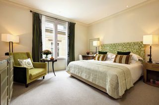 A hotel room with a large bed, a green armchair, a small table with a vase of flowers, and two bedside lamps.