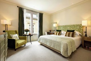 A hotel room with a bed, a chair, a small table with a vase, and a nightstand with a lamp.
