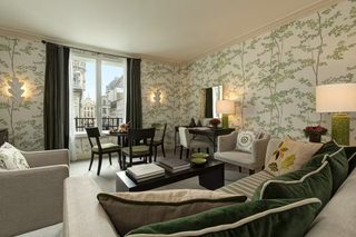 A well-lit hotel room with a dining area, a sofa, and a view of a historic building through the window.