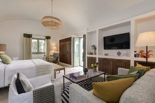 A hotel room with a bed, a sofa, a coffee table, a TV, and a lamp.