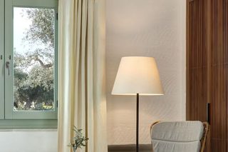 A bedroom with a bed, a wicker chair, a small table with a vase, and a lamp.