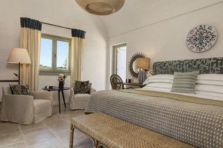 A bedroom with a bed, a chair, a table, and a lamp.