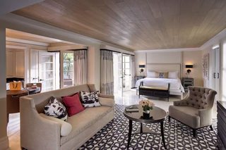 A spacious hotel room with a large bed, a sofa, a chair, and a dining area.