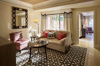 A living room with a beige sofa, a pink armchair, a round coffee table, and a patterned rug.