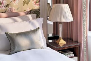 A neatly made bed with white linens, a green pillow, and a bedside table with a lamp and books.