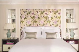 A neatly made bed with a floral headboard, bedside tables with lamps, and a bookshelf with books.