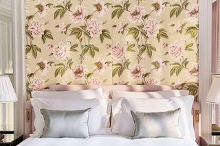 A hotel room with a floral wallpaper, a bed with white linens, and two bedside lamps.
