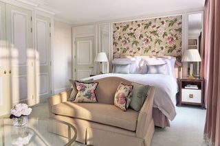 A bedroom with a bed, a sofa, a glass coffee table, a nightstand, and a mirror.