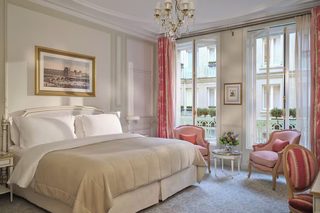 A hotel room with a large bed, a chandelier, a painting, and a view of the city through large windows.