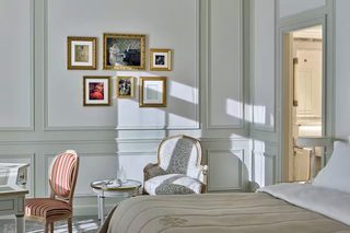 A bedroom with a bed, two chairs, a small table, and a wall with framed pictures.