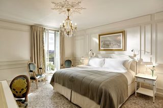 A spacious bedroom with a large bed, a chandelier, a framed picture, and a view of the outdoors.