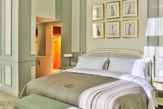 A neatly made bed with a white and beige bedspread, a wooden headboard, and a footboard. There are framed pictures on the wall above the bed.
