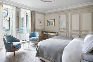 A hotel room with a bed, two armchairs, a desk, and a view of the outside.