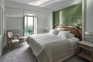 A hotel room with a large bed, a chair, a small table, and a view of the city through a large window.