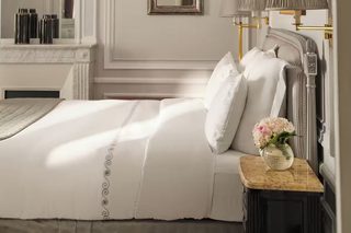 A hotel room with a large bed, a bedside table with a lamp, a mirror, and a vase with flowers.
