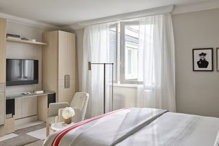 A hotel room with a bed, a desk, a chair, a TV, and a window with curtains.