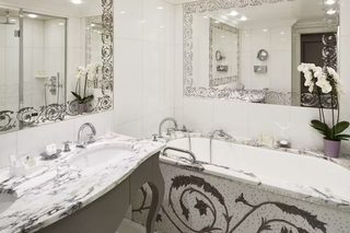 A modern bathroom with a large bathtub, two sinks, and ornate mirrors.