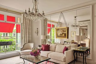 A spacious living room with a white sofa, a glass coffee table, and a chandelier.