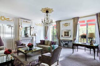 A classic, elegantly furnished living room with a chandelier, comfortable seating, and a view through large windows.