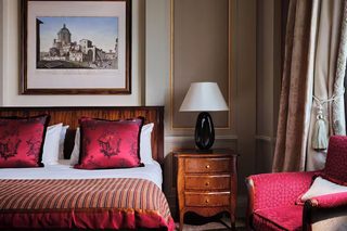 A hotel room with a bed, a nightstand, a lamp, a chair, and a framed picture on the wall.