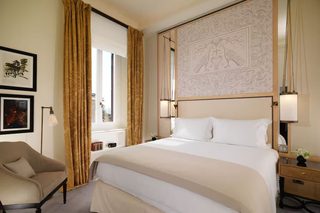 A hotel room with a large bed, a chair, a nightstand, and a wall with an ornate design.