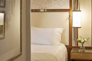 A hotel room with a bed, a nightstand with a lamp, and a wall with a decorative pattern.