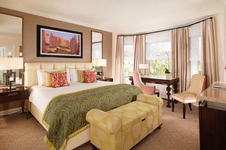 A hotel room with a large bed, a desk, a chair, a sofa, and a window with curtains.