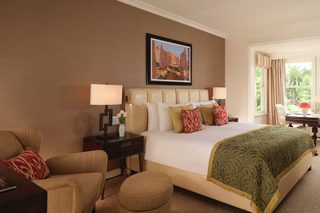 A hotel room with a large bed, two bedside tables, a chair, a desk, and a window with curtains.