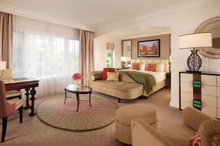 A hotel room with a sofa, armchair, round table, and a bed with a green throw.