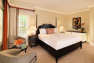 A hotel room with a four-poster bed, a sitting area with a chair and a table, and a nightstand with lamps.