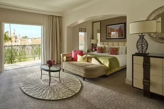 A hotel room with a bed, a sofa, a round rug, a desk, and a view of a building outside.