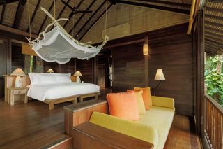 A wooden cabin with a bed, a sofa, and a hanging hammock.
