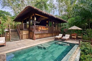 A wooden deck with a pool, lounge chairs, and a thatched-roof structure.