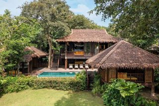 A resort with multiple thatched-roof structures, a central pool, and lush greenery.