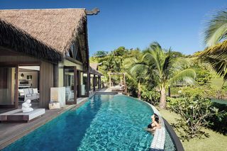 A poolside area with a thatched-roof building, a lounge with seating, and lush greenery.