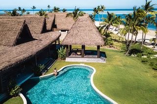 A resort with a swimming pool, thatched-roof structures, and a beach view.