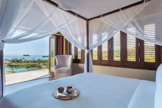 A bedroom with a large bed, a chair, and a view of a pool and ocean.