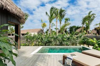 A pool area with a wooden deck, lounge chairs, and a thatched-roof building.